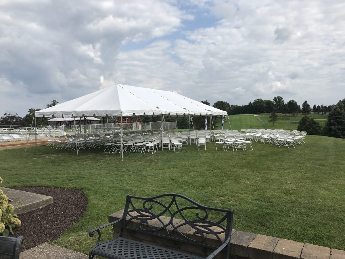 Wedding ceremony setup on a country-club lawn with white chairs, aisle, and a 20x40 frame tent